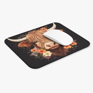 May include: A black mouse pad with a brown and white Highland cow with a floral wreath around its head. The cow is looking directly at the viewer.