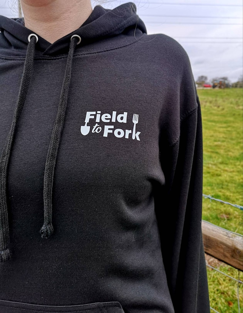 May include: Black hooded sweatshirt with a white logo that says "Field to Fork" with a shovel and fork graphic.