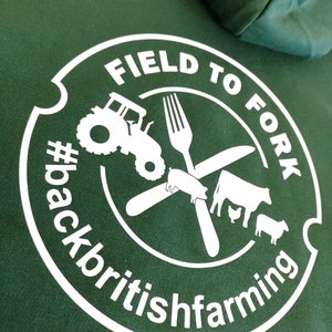 May include: White graphic on a green hoodie with a circle containing the text "FIELD TO FORK #backbritishfarming" and a tractor, fork, knife, pig, cow, chicken, and sheep.