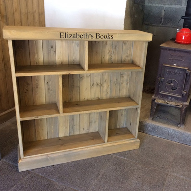 May include: A wooden bookshelf with multiple shelves and compartments. The bookshelf is made of natural wood with a light brown finish. The top shelf has the text "Elizabeth's Books" printed on it.