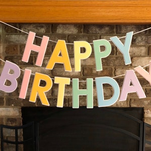 HAPPY BIRTHDAY banner made with pastel cardstock. Background made from white cardstock. Letters are cut out of different colors of sturdy cardstock. These are attached with 3d tape. Letters are strung together with white ribbon. There is extra ribbon on the ends for you to hang it up.