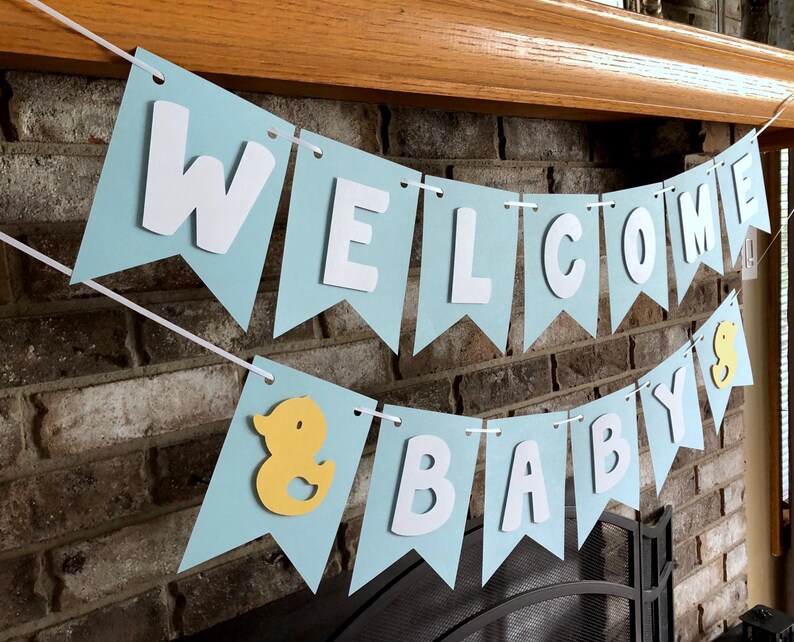 Rubber duck Welcome Baby sign. The flags are made with light blue cardstock backgrounds and white letters. The letters are attached with 3d tape to give it dimension. The two end flags are decorated with yellow rubber ducks. These are strung on a coordinating satin ribbon with plenty of extra to hang the banner.