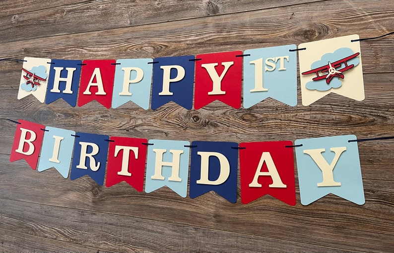 Vintage airplane Happy Birthday banner. Alternating navy blue, red and light blue cardstock flags. Ivory letters are attached with 3D tape. 3D airplanes decorate the two end flags. The banner is strung on a matching ribbon ready to hang.