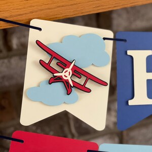 Close up image of 3D vintage airplane on an ivory cardstock flag. There are 2 clouds in the background.