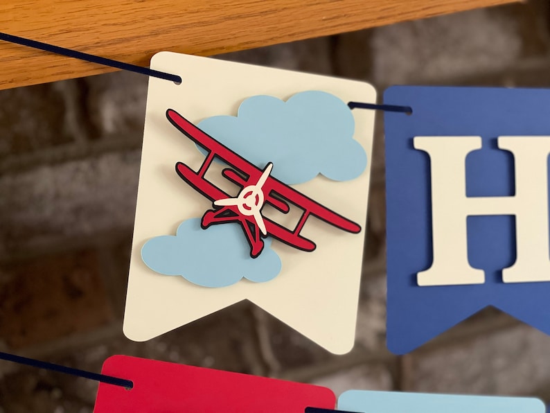 Close up image of 3D vintage airplane on an ivory cardstock flag. There are 2 clouds in the background.