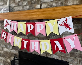 May include: A red, yellow, pink, and white banner with the words "HAPPY BIRTHDAY" in white letters. The banner has a lobster design on each end.