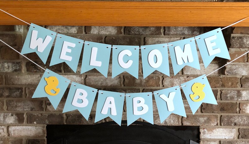 Rubber duck Welcome Baby sign. The flags are made with light blue cardstock backgrounds and white letters. The letters are attached with 3d tape to give it dimension. The two end flags are decorated with yellow rubber ducks. These are strung on a coordinating satin ribbon with plenty of extra to hang the banner.