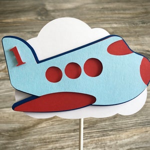 May include: Blue and red airplane cake topper with a white cloud and the number "1" on the side.