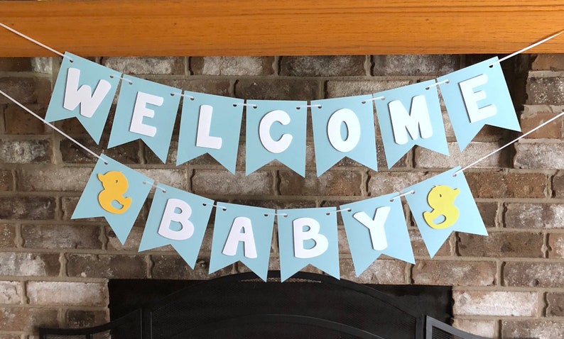 Rubber duck Welcome Baby sign. The flags are made with light blue cardstock backgrounds and white letters. The letters are attached with 3d tape to give it dimension. The two end flags are decorated with yellow rubber ducks. These are strung on a coordinating satin ribbon with plenty of extra to hang the banner.