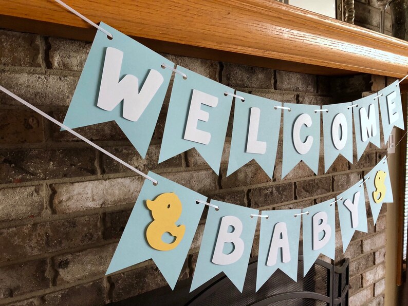 Rubber duck Welcome Baby sign. The flags are made with light blue cardstock backgrounds and white letters. The letters are attached with 3d tape to give it dimension. The two end flags are decorated with yellow rubber ducks. These are strung on a coordinating satin ribbon with plenty of extra to hang the banner.