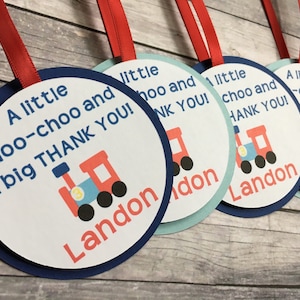 May include: A set of four round, blue and white thank you tags with a red train illustration and the text "A little choo-choo and a big THANK YOU!" with the name Landon printed below the train.
