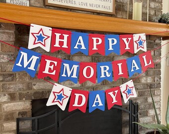 May include: A red, white, and blue banner with the words "Happy Memorial Day" hanging above a fireplace. The banner is made of paper and has stars on each end.