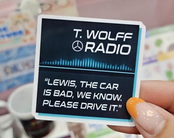 Könnte beinhalten: Ein quadratischer Aufkleber mit dunklem Hintergrund, weißem Text T. WOLFF RADIO, einer blauen Schallwellengrafik und dem Zitat "LEWIS, THE CAR IS BAD, WE KNOW. PLEASE DRIVE IT." Der Aufkleber hat einen dünnen weißen Rand und eine blaue Linie.