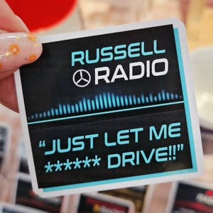 May include: A square sticker with the text "RUSSELL RADIO" in white and teal. Below the text is a graphic of sound waves and the phrase "JUST LET ME ***** DRIVE!!!" in teal. The sticker is held by a hand.
