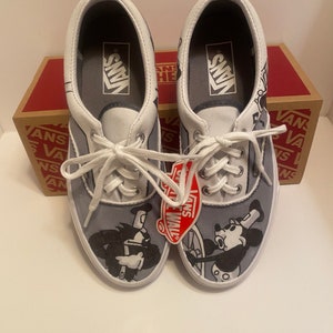 May include: Pair of Vans Era sneakers with a gray and white design. The shoes feature a cartoon graphic of Mickey Mouse and another character. The Vans logo is visible on the tongue and insole. The shoes are new with tags.