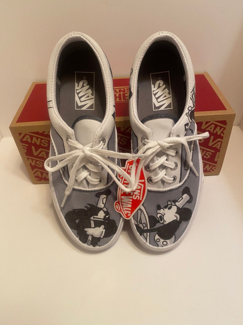 May include: Pair of Vans Era sneakers with a gray and white design. The shoes feature a cartoon graphic of Mickey Mouse and another character. The Vans logo is visible on the tongue and insole. The shoes are new with tags.