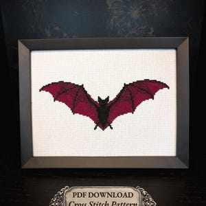 Può includere: Uno schema a punto croce incorniciato raffigurante un pipistrello con corpo nero e ali color magenta scuro su uno sfondo a griglia bianco. Una targa decorativa sottostante riporta: PDF DOWNLOAD, Cross Stitch Pattern, 5x7" Finished Size.