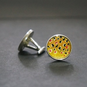 Może przedstawiać: Para srebrnych spinek do mankietów z okrągłym, żółtym, czarnym i czerwonym wzorem. Wzór przypomina rybę.