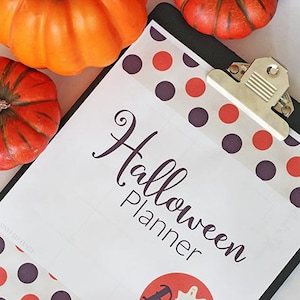 May include: A black clipboard with a white sheet of paper that says "Halloween Planner" in a decorative font. The paper has a border of orange and purple polka dots. There are three small orange pumpkins on the clipboard.