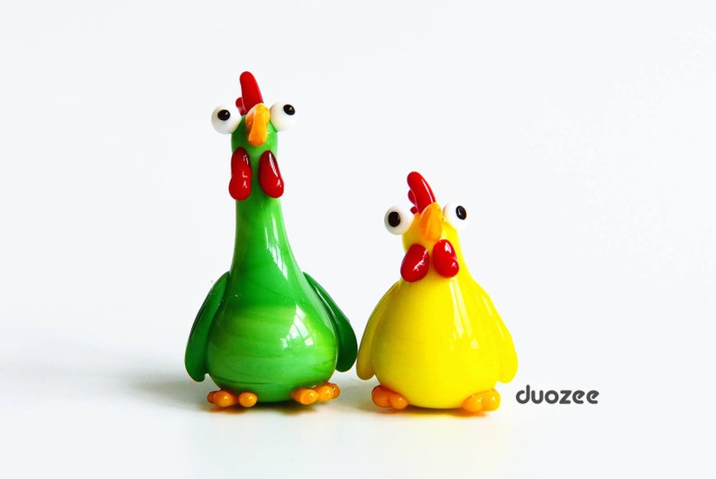 Peut inclure: Deux figurines en verre de poulets aux grands yeux. Un poulet est vert et l'autre est jaune.