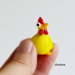 Peut inclure: Une petite figurine en verre d'un poulet jaune avec une cr&ecirc;te et un bec rouges. Le poulet a des yeux blancs et tient la t&ecirc;te haute.