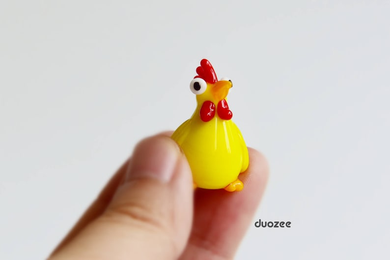 Peut inclure: Une petite figurine en verre d'un poulet jaune avec une cr&ecirc;te et un bec rouges. Le poulet a des yeux blancs et tient la t&ecirc;te haute.