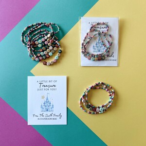 May include: Three sets of colorful beaded bracelets featuring letter beads that spell words like FANTASY, MAGIC, WANDER, ADVENTURE, DESTINY, DREAM, and TREASURE. Two sets are accompanied by white cards with a castle illustration and text.
