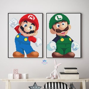 May include: Two framed pixel art prints of Mario and Luigi characters from the Super Mario Bros. video game series. The prints are hanging on a white wall above a white wooden shelf with a white rabbit figurine, a black and white striped pillow, and a gray star-shaped light.