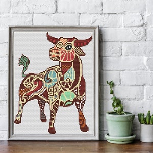 May include: A colourful cross-stitch pattern of a bull, with intricate details and a white background. The bull is brown, red, yellow, green, and blue.