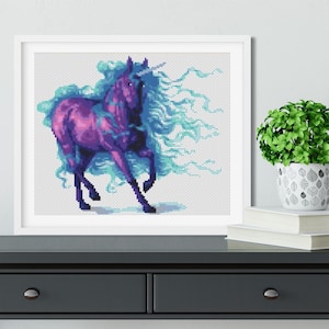 May include: A framed cross-stitch artwork depicting a purple unicorn with a blue mane and tail. The unicorn is standing on a white background.