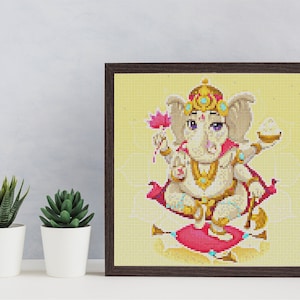 May include: A framed diamond painting of a cartoon depiction of the Hindu deity Ganesha. Ganesha is depicted as a white elephant with a red lotus flower in one hand and a sweet in the other. He is wearing a gold crown and jewelry and sitting on a pink cushion.