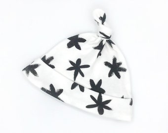 May include: White baby hat with a black and white floral pattern. The hat has a knot on top.