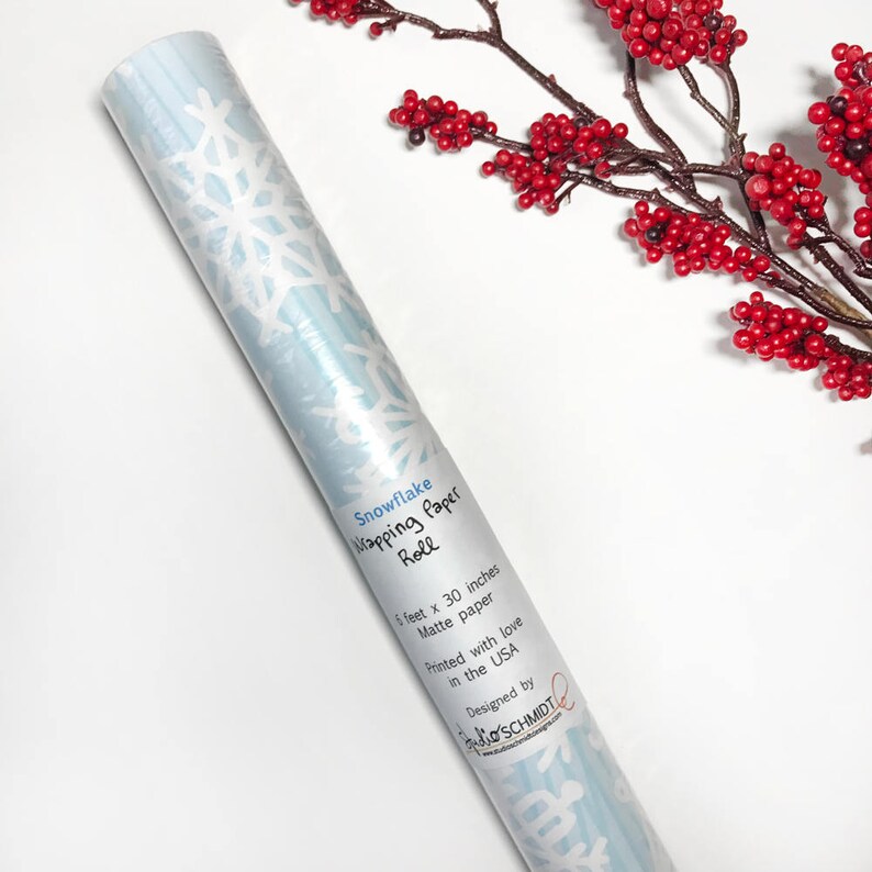 May include: A roll of blue snowflake wrapping paper with white snowflakes. The paper is 1 foot by 30 inches and is matte. It says "Snowflake Wrapping Paper Roll" and "Printed with love in the USA" and "Designed by Jo-Ann Schmidt".