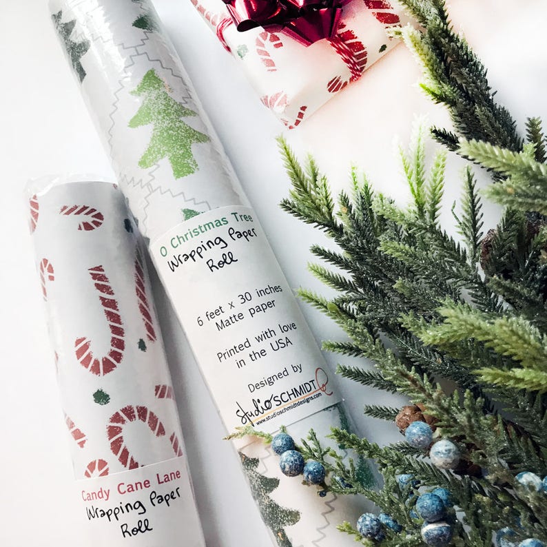 May include: Two rolls of Christmas wrapping paper. One roll features a green Christmas tree design and the other features a red and white candy cane design. Both rolls are 6 feet by 30 inches and are printed with love in the USA. The text on the rolls reads "O Christmas Tree Wrapping Paper Roll" and "Candy Cane Lane Wrapping Paper Roll".