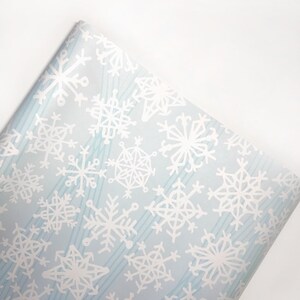 May include: Blue wrapping paper with a white snowflake pattern. The snowflakes are of various sizes and shapes.