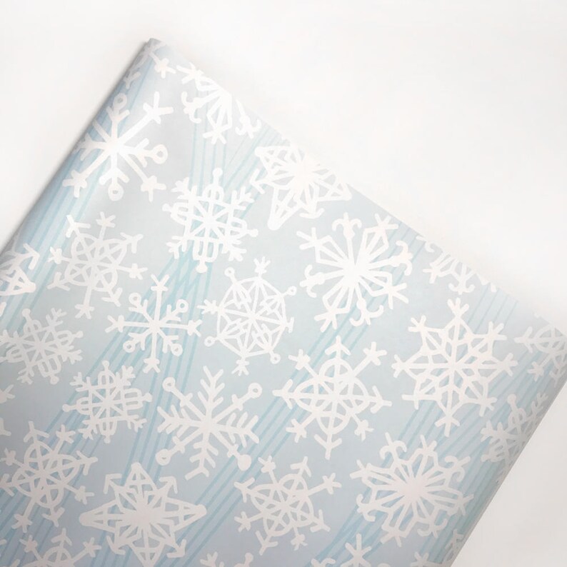 May include: Blue wrapping paper with a white snowflake pattern. The snowflakes are of various sizes and shapes.