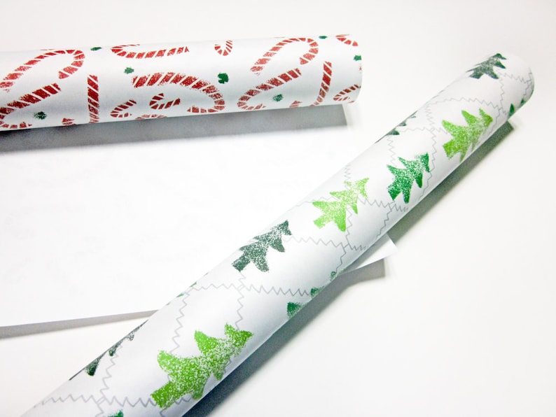 May include: Two rolls of white wrapping paper with different Christmas designs. One roll has red candy canes and the other has green Christmas trees.