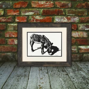 May include: Black and white print of a donkey with its head down, framed in a dark wood frame.