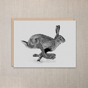 May include: Black and white illustration of a running hare on a white background. The hare is in mid-stride, with its legs extended and ears perked up. The artwork is on a rectangular card with a tan border.