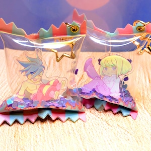 May include: Two clear plastic pouches with gold chains, each containing a colorful cartoon character and glitter. The pouches are decorated with pink, blue, and green stripes.