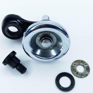 May include: A silver-toned bicycle derailleur with a black lever and a small black screw. The derailleur has a round, silver-toned housing with a small hole in the center. There are two small, black washers.