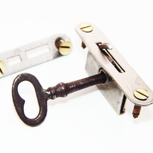 May include: A vintage key and lock set with a brass key and a silver lock. The lock has a small lever and a keyhole. The key is rusty and has a heart-shaped bow.