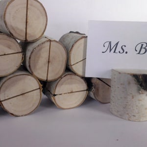Puede incluir: Un conjunto de seis porta tarjetas de mesa de madera de abedul natural. Los soportes están apilados en forma de pirámide. Una tarjeta blanca con texto negro dice "Sra. Birch".