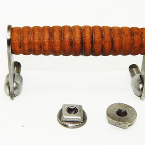 Könnte beinhalten: Ein Griff im Vintage-Stil mit einem braunen, geriffelten Holzgriff und Metallhalterungen. Der Griff ist mit zwei Metallhalterungen und Schrauben zur Montage ausgestattet. Zwei Metallmuttern sind ebenfalls enthalten.