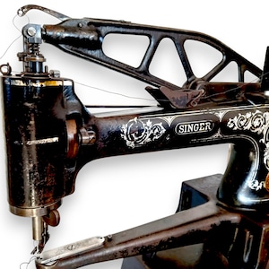May include: Close-up of a vintage Singer sewing machine. The machine is black with ornate white floral detailing and the Singer logo. The needle and thread are visible, and the machine has a large, curved arm.