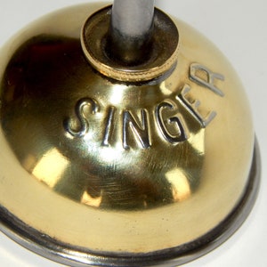 K&ouml;nnte beinhalten: Eine goldfarbene &Ouml;ldose mit silbernem Deckel und dem eingepr&auml;gten Wort "SINGER" an der Seite.