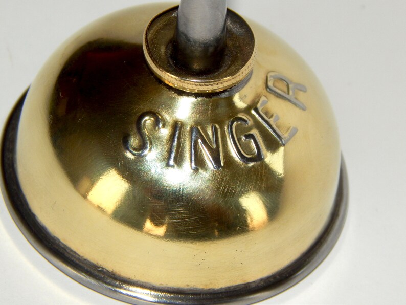 K&ouml;nnte beinhalten: Eine goldfarbene &Ouml;ldose mit silbernem Deckel und dem eingepr&auml;gten Wort "SINGER" an der Seite.