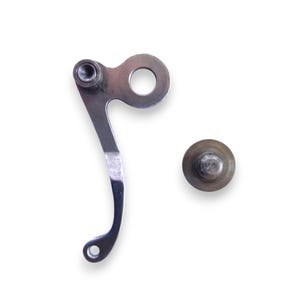 May include: Two metal machine parts on a white background. One part is a curved, silver lever with a hole at each end and a circular opening. The other part is a small, round, silver screw.