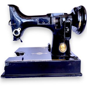 May include: A vintage black Singer sewing machine with gold accents. The machine features a curved arm, a circular handwheel, and a rectangular base. The Singer logo is visible on the front. The machine is in good condition.