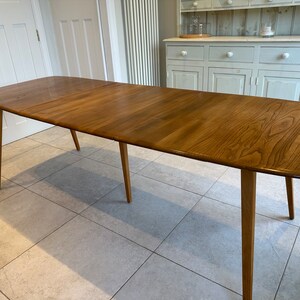 May include: A wooden dining table with a light brown finish. The table has a rectangular top with rounded corners and four tapered legs. The table is approximately 183 cm long.